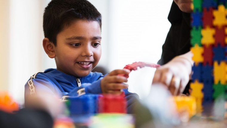 A young boy playing with toys while his mum watches over him
