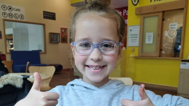 Young girl smiling and wearing glasses. Her thumbs are up.
