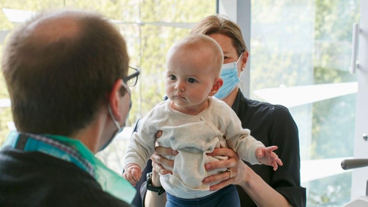A clinician giving a baby an eye exam. The mum is holding the baby.
