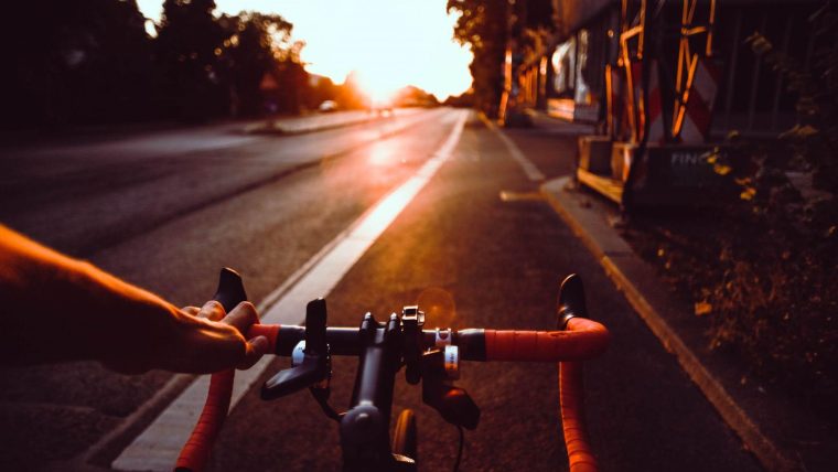 a view of a road from the perspective of a cyclist looking over their handlebars and cycling towards a sunset